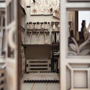 Puede incluir: Un diorama de madera en miniatura de un interior de taberna con detalles cortados con l&aacute;ser. Las paredes muestran un mapa, jarras colgantes y cucharones. Una caja de madera se asienta en el suelo cerca de una alfombra con dise&ntilde;o de br&uacute;jula.
