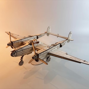 Puede incluir: Maqueta de avión de madera con dos fuselajes, alas y hélices. El modelo está hecho de madera clara y presenta cortes y marcas detalladas. El avión tiene un diseño clásico con una hélice en cada ala.