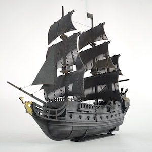 May include: A detailed model of a tall ship with black sails and a dark gray hull. The ship has multiple masts and sails, with intricate detailing on the hull and rigging. The figurehead is gold.
