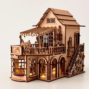 May include: A miniature wooden coffee shop model with intricate details. The two-story structure features a balcony, arched windows, and a staircase. The sign reads "Coffee". Warm lights illuminate the interior, creating a cozy ambiance.