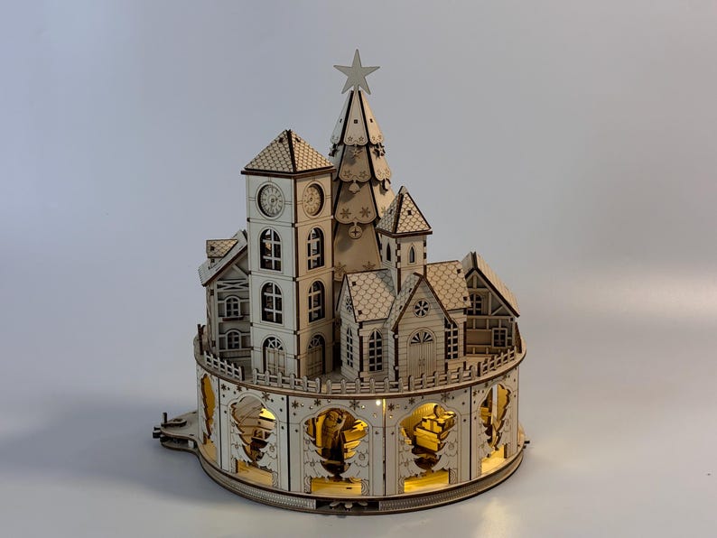 May include: A wooden Christmas village with a clock tower, houses, and a Christmas tree. The village has intricate details, including windows, doors, and decorative cutouts. It is illuminated with warm, inviting lights, and a star sits atop the tree.