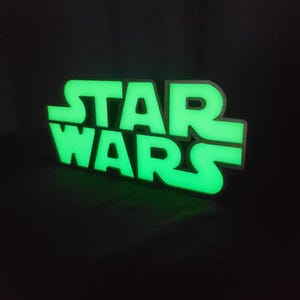 Op de afbeelding: Een groen verlicht bord met de woorden "STAR WARS" in een vet, bloklettertype.