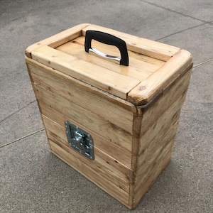 Può includere: Una scatola di legno per la conservazione con una maniglia nera e una chiusura in metallo. La scatola è realizzata in legno riciclato e ha una finitura naturale.