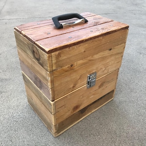 Può includere: Una scatola di legno con una maniglia nera e un chiavistello argentato. La scatola è realizzata in legno riciclato e ha un aspetto rustico.