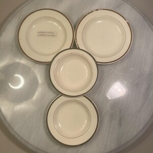 May include: Four cream-coloured ceramic bowls with a brown rim. One bowl features a small rectangular label with the text WEDGWOOD CREAMWARE. The bowls have a smooth, rounded design and are arranged in a cluster on a circular surface.