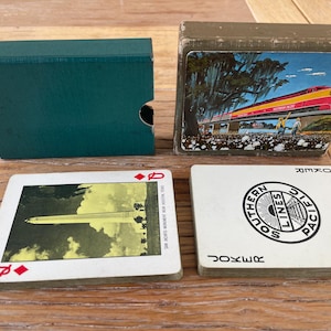 May include: Two decks of playing cards with cases. One case is solid teal, the other features a Southern Pacific train illustration. One card shows the San Jacinto Monument, and the other is a Joker card with the Southern Pacific Lines circular logo.