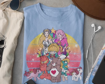 May include: A light blue t-shirt with a retro-style graphic featuring cartoon characters from popular 80s shows, including Care Bears, My Little Pony, and Garfield. The graphic is set against a sunset background with stars and rainbows.
