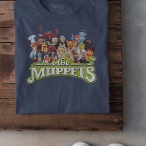 May include: A navy blue t-shirt with a vintage-style graphic of the Muppets characters. The text "The Muppets" is printed in green and white below the characters.