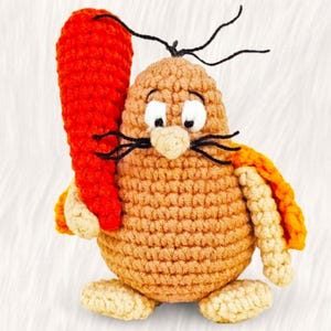 May include: A crocheted mole plush toy holding a carrot. The mole is brown with a yellow and orange cape. The mole has black eyes, a black nose, and a black moustache.