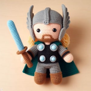 以下が含まれることがあります： マーベルコミックのソーの、かぎ針編みで作ったぬいぐるみ。おもちゃは、翼のついた灰色のヘルメット、黒と灰色の鎧、緑色のマントを着ています。おもちゃは青い剣を持っています。