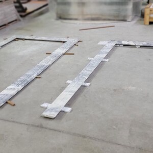 May include: Two rectangular frames made of white marble tiles are laid out on a concrete floor. The frames are made of individual tiles that are arranged in a grid pattern. The frames are positioned at a 90-degree angle to each other.