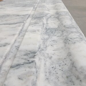 May include: Close-up of a white marble countertop with a decorative edge detail. The marble has a subtle gray veining pattern.