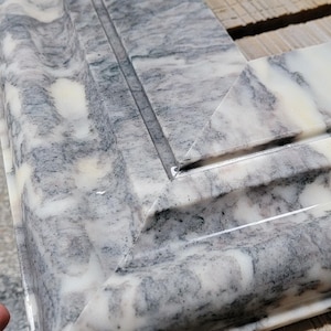 May include: Close-up of a corner of a white marble tile with gray veining. The tile has a beveled edge and a polished finish.