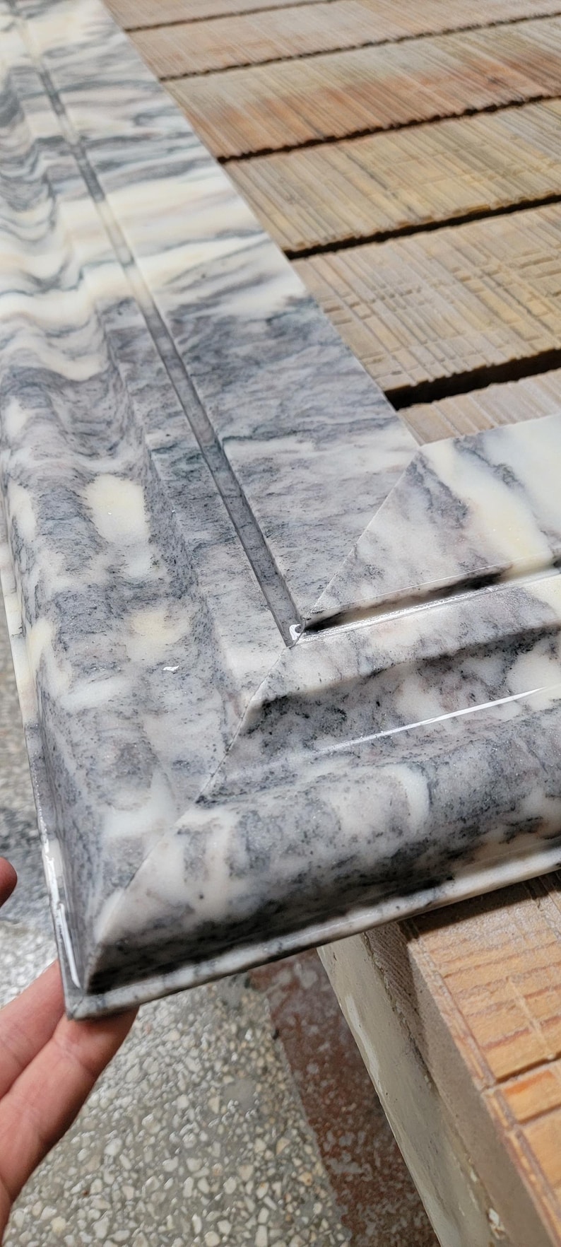 May include: Close-up of a corner of a white marble tile with gray veining. The tile has a beveled edge and a polished finish.