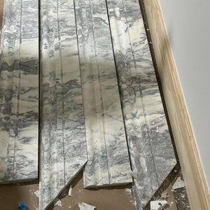 May include: Close-up of several pieces of gray and white marble tile with a decorative pattern. The tiles are cut at an angle and have rough edges.