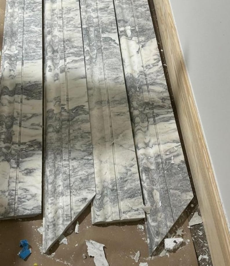 May include: Close-up of several pieces of gray and white marble tile with a decorative pattern. The tiles are cut at an angle and have rough edges.