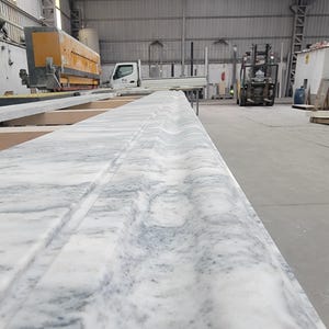 May include: Close-up of a white marble countertop with a decorative edge detail. The countertop is in a workshop setting.