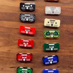May include: A collection of colorful, miniature cassette tape-shaped objects. Each tape features the word "WOUNDS" and a skull graphic. The tapes are in various colors, including black, orange, clear, beige, red, green, and blue, with numbers displayed.