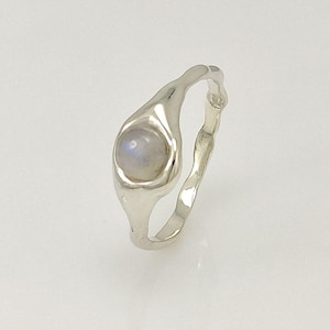 Puede incluir: Un anillo de plata con una piedra de luna engastada en una banda única de forma orgánica.