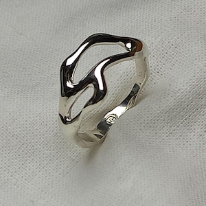 May include: A polished silver ring featuring an open, fluid, and irregular organic shape. The band has a smooth, reflective surface with a distinct cutout design that creates a continuous, flowing silhouette around the finger. A small hallmark is visible.