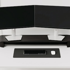 K&ouml;nnte beinhalten: Ein dunkelbrauner Monitorst&auml;nder aus Holz mit pillenf&ouml;rmiger Platte und geriffelten Seitenst&uuml;tzen, der zwei schwarze Computermonitore mit wei&szlig;en Standf&uuml;&szlig;en tr&auml;gt. Darunter befindet sich eine schwarze Schreibtischunterlage mit Tastatur.