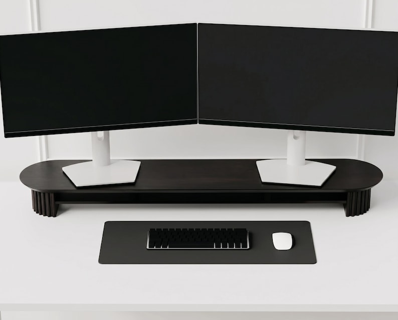 K&ouml;nnte beinhalten: Ein dunkelbrauner Monitorst&auml;nder aus Holz mit pillenf&ouml;rmiger Platte und geriffelten Seitenst&uuml;tzen, der zwei schwarze Computermonitore mit wei&szlig;en Standf&uuml;&szlig;en tr&auml;gt. Darunter befindet sich eine schwarze Schreibtischunterlage mit Tastatur.