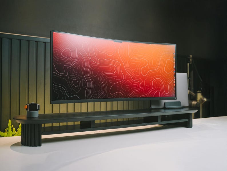 May include: A black curved monitor with a red and orange abstract design on the screen sits on a black monitor stand with a shelf. The stand is on a white surface.