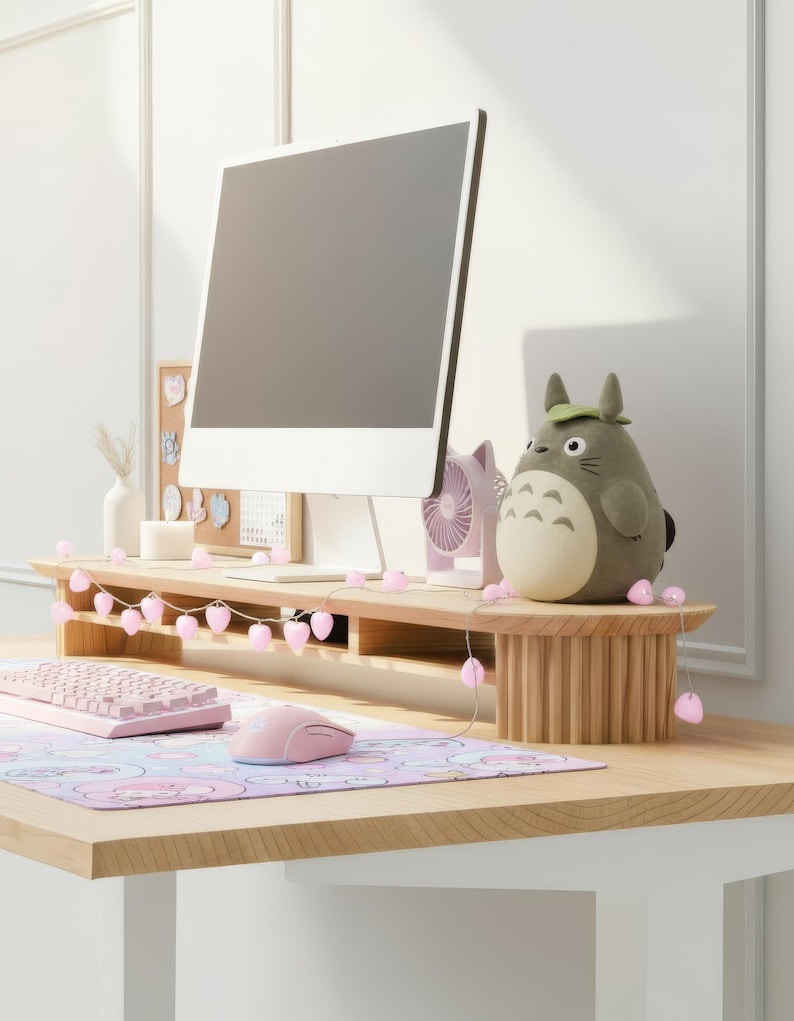 K&ouml;nnte beinhalten: Ein Monitorst&auml;nder aus hellem Holz mit geriffeltem Sockel, auf dem ein Computermonitor, ein kleiner Totoro-Pl&uuml;sch, ein rosa Ventilator und eine Lichterkette mit rosa Herzen stehen. Eine rosa Tastatur und Maus liegen auf einer gemusterten Schreibtischunterlage.