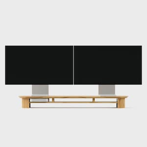 K&ouml;nnte beinhalten: Ein langer Monitorst&auml;nder aus hellem Holz mit einem geriffelten Lamellendesign an den beiden Endst&uuml;tzen. Der St&auml;nder verf&uuml;gt &uuml;ber eine horizontale Ablagefl&auml;che und tr&auml;gt zwei schwarze Computermonitore nebeneinander, mit einem kleinen silbernen Ger&auml;t darunter.