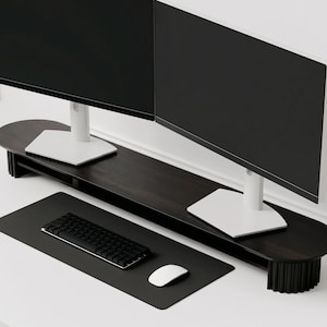 K&ouml;nnte beinhalten: Ein langer Monitorst&auml;nder aus dunklem Holz mit abgerundeten Enden und geriffelten, vertikalen St&uuml;tzen. Der St&auml;nder tr&auml;gt zwei schwarze Computermonitore mit wei&szlig;en Sockeln. Darunter befindet sich eine schwarze Schreibtischunterlage mit Tastatur und Maus.
