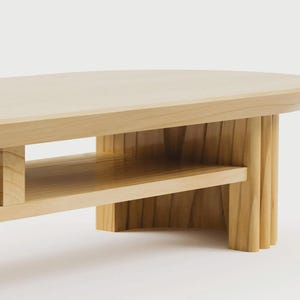 K&ouml;nnte beinhalten: Ein heller Couchtisch aus Holz mit einer glatten, ovalen Tischplatte und einer unteren Ablage. Der Tisch verf&uuml;gt &uuml;ber dicke, vertikal geriffelte Beine, die f&uuml;r strukturelle Stabilit&auml;t sorgen und die nat&uuml;rliche Maserung des Holzes zeigen.