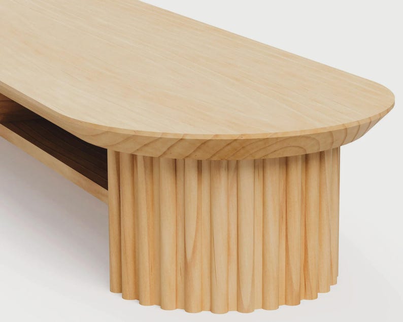 K&ouml;nnte beinhalten: Ein Couchtisch aus hellem Holz mit einer glatten, ovalen Tischplatte und einem zylindrischen Sockel mit vertikaler Rillenstruktur. Der Tisch weist eine sichtbare Holzmaserung sowie eine Ablagefl&auml;che unterhalb der Hauptoberfl&auml;che auf.