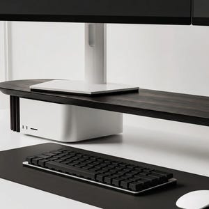 K&ouml;nnte beinhalten: Ein Monitorst&auml;nder aus dunklem Holz mit wei&szlig;em Fu&szlig; und vertikalen Seitenlamellen, der einen Computermonitor tr&auml;gt. Unter dem St&auml;nder steht ein wei&szlig;er Computer. Eine schwarze Tastatur und eine wei&szlig;e Computermaus liegen auf einer schwarzen Schreibtischunterlage.