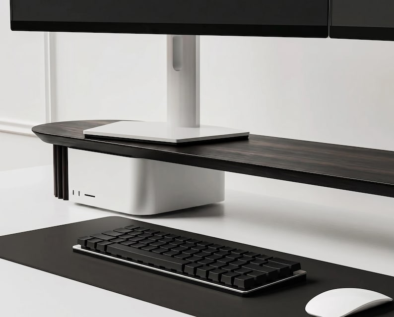 K&ouml;nnte beinhalten: Ein Monitorst&auml;nder aus dunklem Holz mit wei&szlig;em Fu&szlig; und vertikalen Seitenlamellen, der einen Computermonitor tr&auml;gt. Unter dem St&auml;nder steht ein wei&szlig;er Computer. Eine schwarze Tastatur und eine wei&szlig;e Computermaus liegen auf einer schwarzen Schreibtischunterlage.