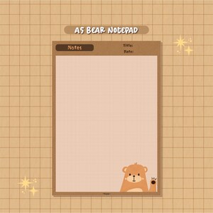 May include: A brown and beige notepad with a grid pattern. The notepad has a brown header with the text "A5 BEAR NOTE PAD" and "Notes". The notepad has a brown border and a cartoon bear peeking out from the bottom right corner.