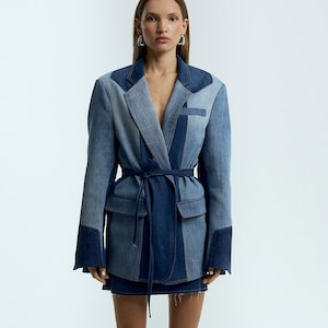 Może przedstawiać: Niebieska kurtka dżinsowa z patchworkowym wzorem, z paskiem w talii i długimi rękawami. Kurtka jest noszona na dżinsowej spódnicy i w połączeniu z czarnymi kozakami za kolano.