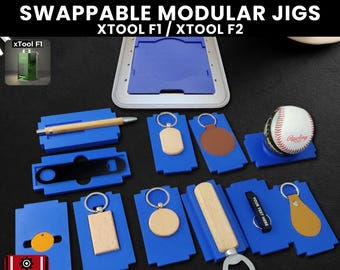 May include: A collection of blue modular jigs with various items, including keychains, a pen, and a baseball. The image includes the text "SWAPPABLE MODULAR JIGS" and "3D JIG SOLUTIONS".