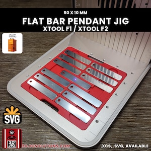 Może przedstawiać: Czerwony przyrząd do zawieszek z płaskich prętów do maszyn laserowych xTool F1 i xTool F2, z otworami na metalowe pręty 50 x 10 mm. Przyrząd jest umieszczony w srebrnej metalowej podstawie, z małym obrazkiem przedstawiającym jednostki xTool F1 i F2.