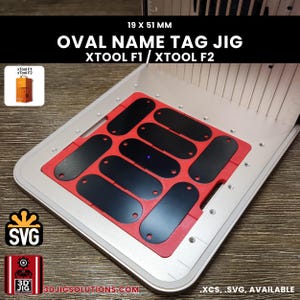 Könnte beinhalten: Eine rote Kunststoffschablone für 19 x 51 mm große ovale Namensschilder für xTool F1 und xTool F2 Lasermaschinen. Die Schablone liegt auf einer silbernen Metallgrundplatte mit Gittermuster und enthält ein kleines Bild der Lasereinheit.