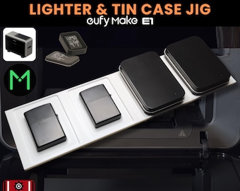 May include: A white jig with two black lighters and two black tin cases. The text "LIGHTER & TIN CASE JIG" and "eufy Make E1" are displayed. The lighter measures 1.5 x 2.2 inches, and the tin case measures 2.4 x 3.3 inches.