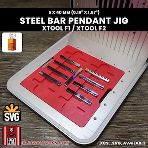 Könnte beinhalten: Eine silberne Stahlstangen-Anhänger-Vorrichtung für xTool F1 und xTool F2 Lasermaschinen, mit einem roten Einsatz mit Schlitzen für 5 x 40 mm Stangen. Die Vorrichtung verfügt über eine metallische Basis mit Ausrichtungsmarkierungen und Beschriftungen.