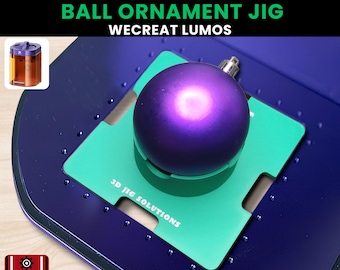 May include: A purple ball ornament sits on a green square within a blue jig. The text "BALL ORNAMENT JIG" and "WECREAT LUMOS" are displayed. The jig is designed for ornaments with sizes 35, 50, 60, 65, and 80 mm. The logo "3D JIG SOLUTIONS" is also visible.
