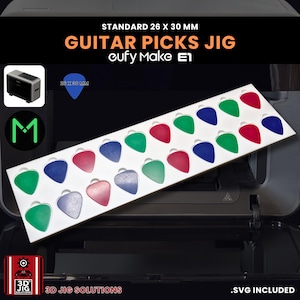 Könnte beinhalten: Eine weiße Vorrichtung mit farbigen Gitarrenplektren in Grün, Rot und Blau. Der Text "GUITAR PICKS JIG" und "STANDARD 26 x 30 mm" sind abgebildet. Das Bild enthält auch den Text "eufy Make E1" und "3D JIG SOLUTIONS".