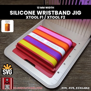 May include: A red silicone wristband jig for xTool F1 and xTool F2 laser machines, featuring a 12 mm width. The jig holds five colorful silicone wristbands in pink, orange, white, purple, and yellow, with the text 3D JIG SOLUTIONS visible.