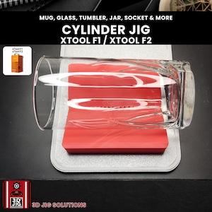 May include: A clear glass tumbler sits on a red cylinder jig, designed for XTOOL F1 and F2 models. The image features the text "CYLINDER JIG" and "XTOOL F1 / XTOOL F2". The product is designed for mugs, glasses, tumblers, jars, sockets, and more.