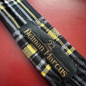 May include: A black, yellow, and white plaid necktie with the "Neiman Marcus" brand label. The tie features a classic plaid pattern with yellow and white stripes on a black background. The label is black with gold lettering.