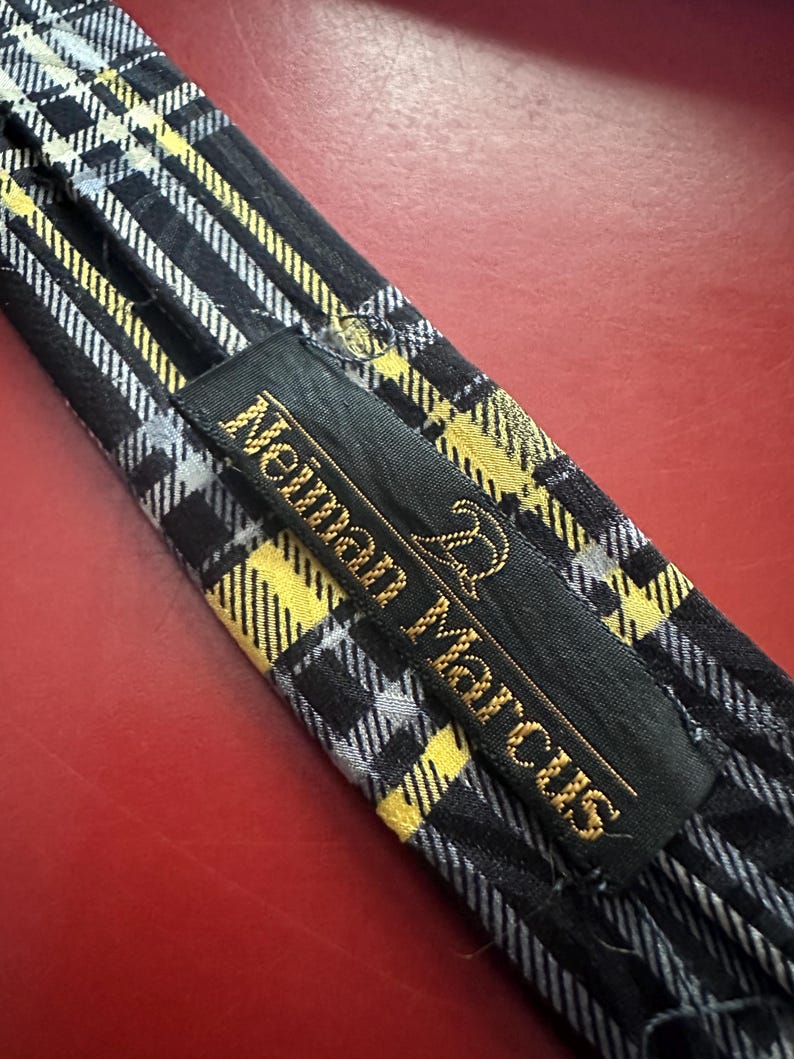 May include: A black, yellow, and white plaid necktie with the "Neiman Marcus" brand label. The tie features a classic plaid pattern with yellow and white stripes on a black background. The label is black with gold lettering.