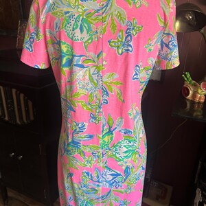 Pode incluir: Vestido rosa de manga curta com um vibrante padr&atilde;o floral em tons de azul, verde e branco. O vestido tem decote em V e uma silhueta reta. O tecido parece ser um tecido de malha leve, adequado para climas quentes.