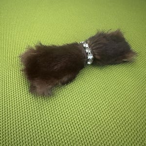 May include: A dark brown fur accessory with a sparkling rhinestone band. The fur is a rich, solid color, and the band is made of clear, glittering stones. The accessory is lying on a green surface.