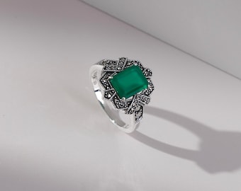 May include: A silver ring with a green gemstone surrounded by a detailed design of small black stones.